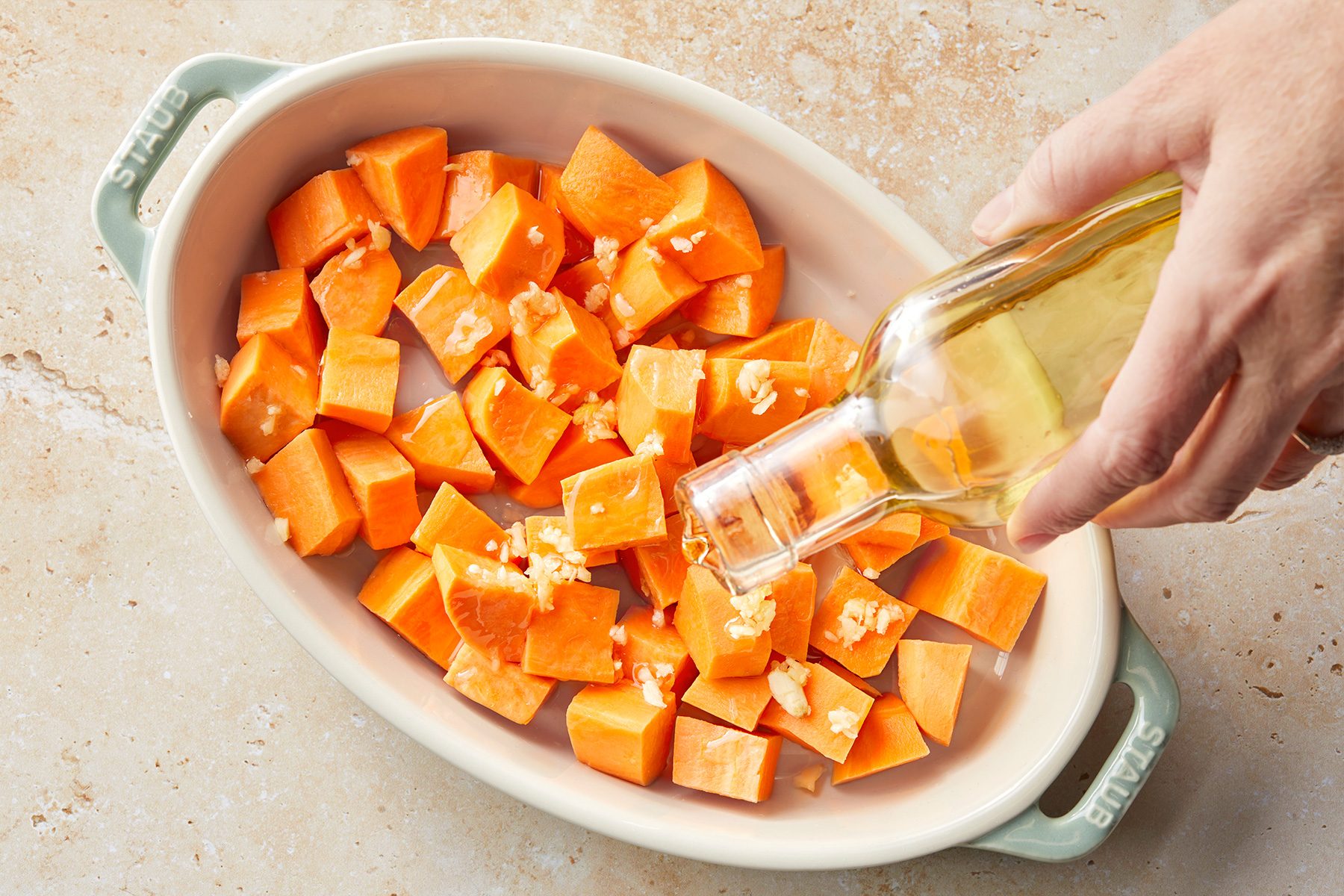 Adding oil to sliced sweet potatoes with garlic and salt, before roasting