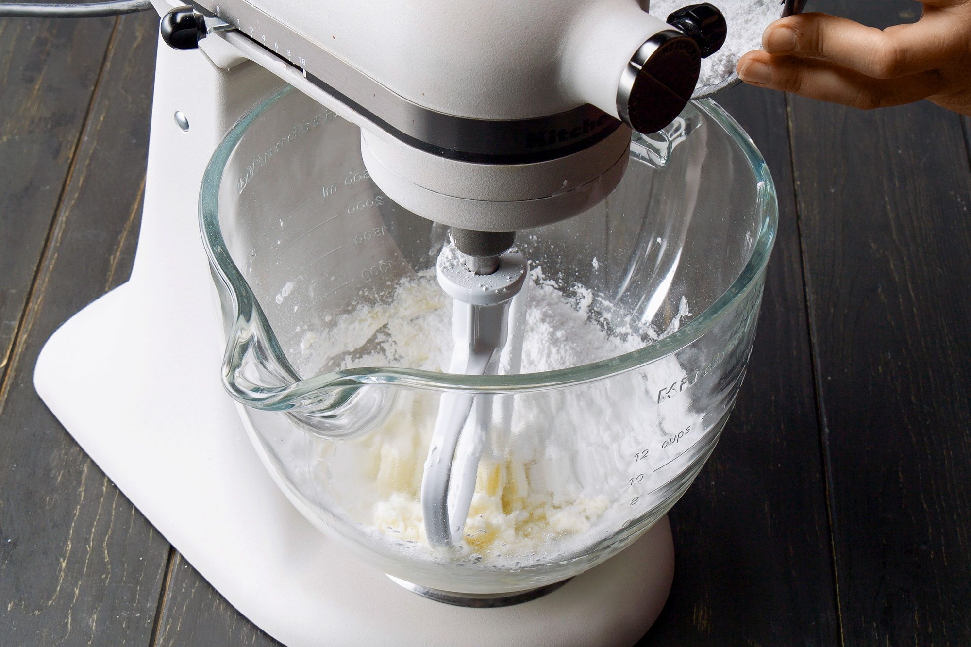 3/4th shot of a stand mixer set against a dark wooden surface; the glass mixing bowl clearly shows the ingredients being blended together
