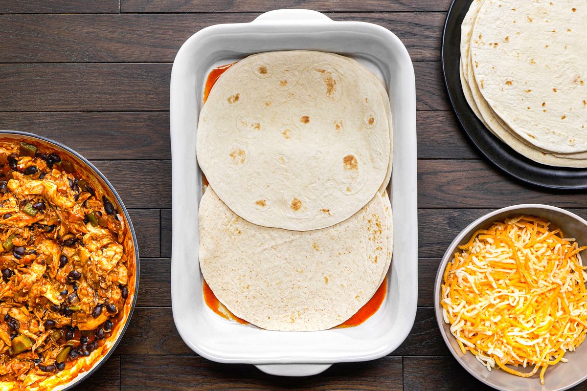 overhead shot of a white rectangular baking dish in the center contains two tortillas layered with red sauce