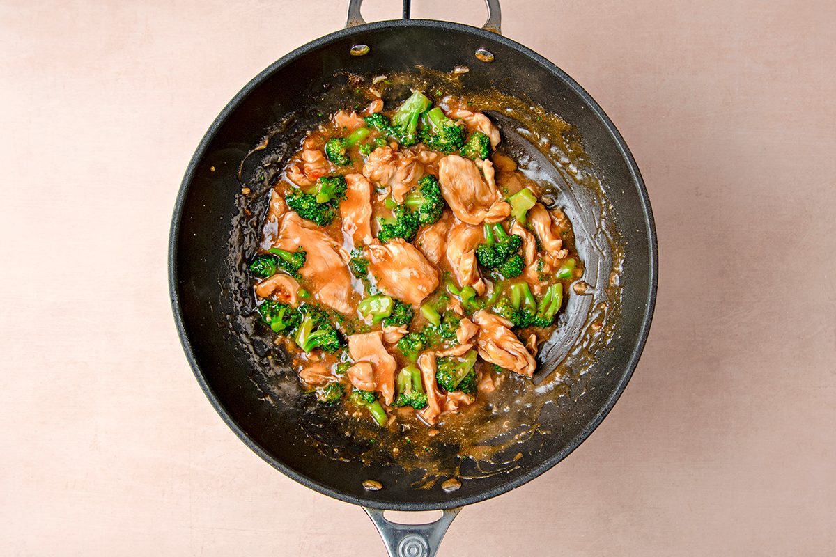 A skillet filled with chicken pieces and broccoli in a brown sauce. The dish is set against a beige background, showcasing its vibrant colors and savory appearance.
