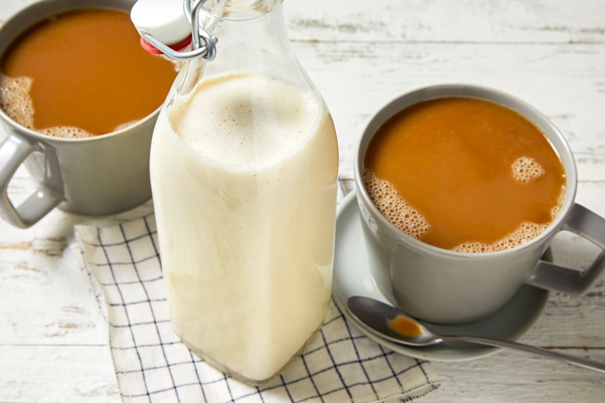 Close shot of Vanilla Coffee Creamer; Store in a glass container; Stir before using; two cups of coffee; spoon; napkin; wooden surface;