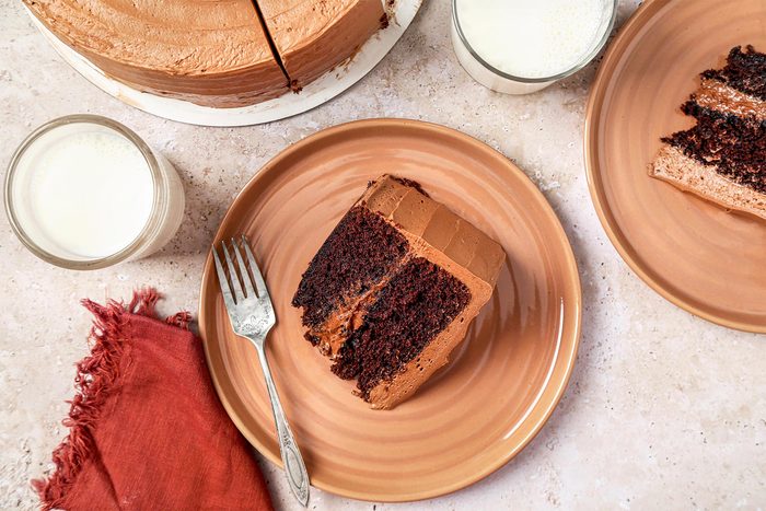 overhead shot of Devil's Food Cake shot on a beige marble surface. Sliced cake served on tan plates with milk.