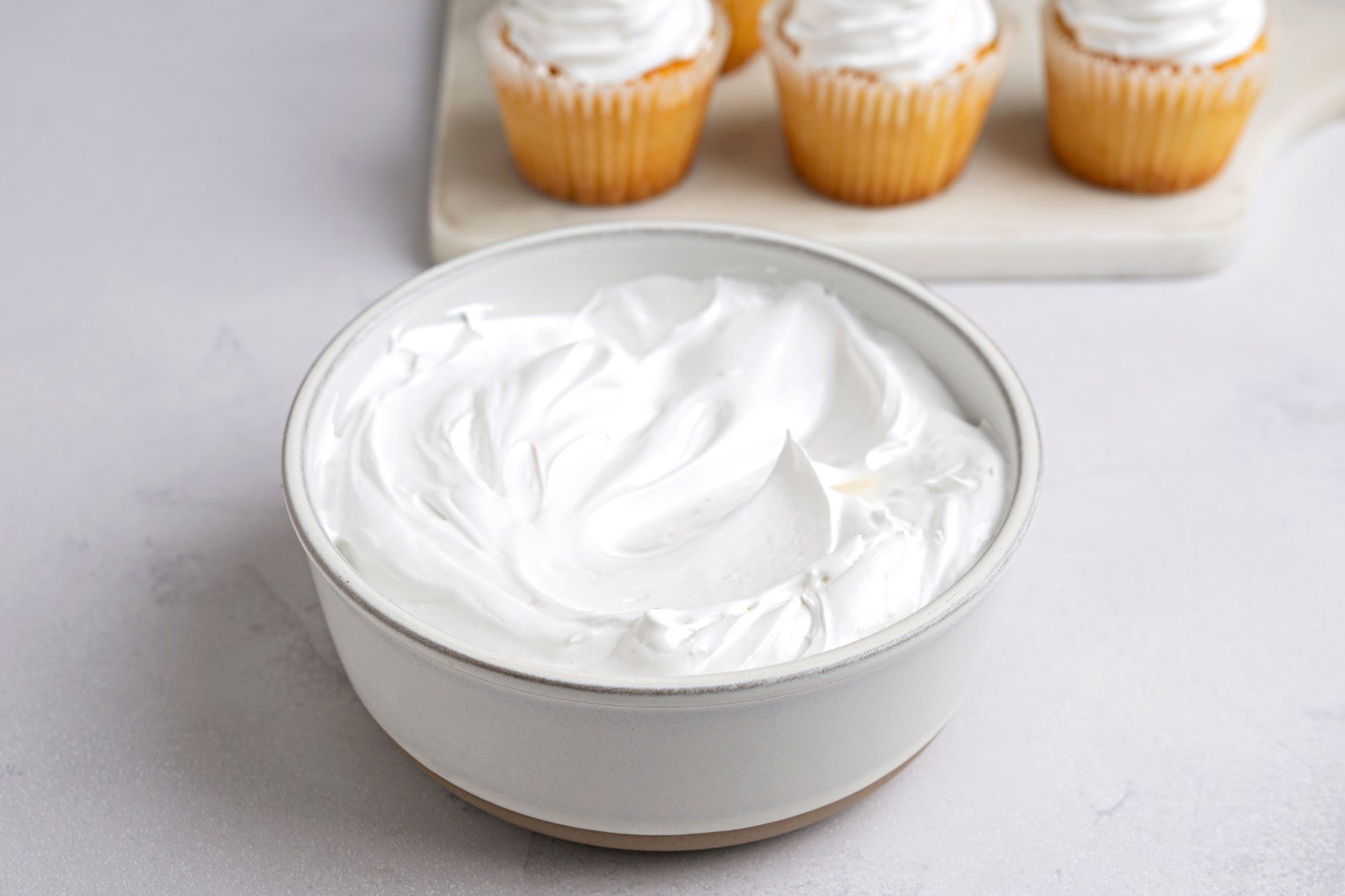 Table view shot of Fluffy White Frosting; in a large bowl; spatula; marble surface;