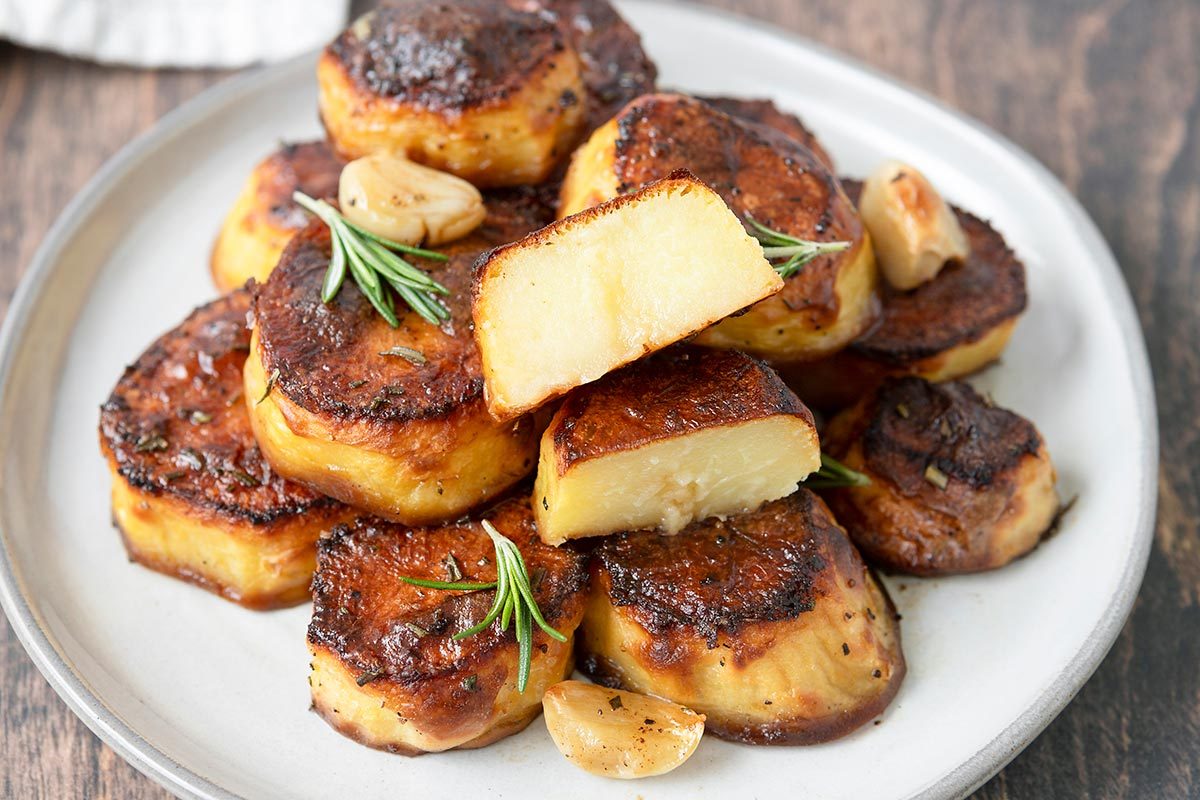 Fondant potatoes served on a plate, with one potato being cut open on top.