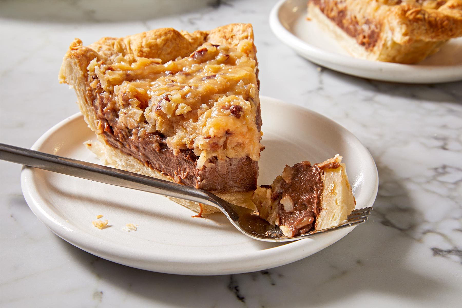 Close up shot of German Chocolate Pie slice kept on a white plate with a fork.