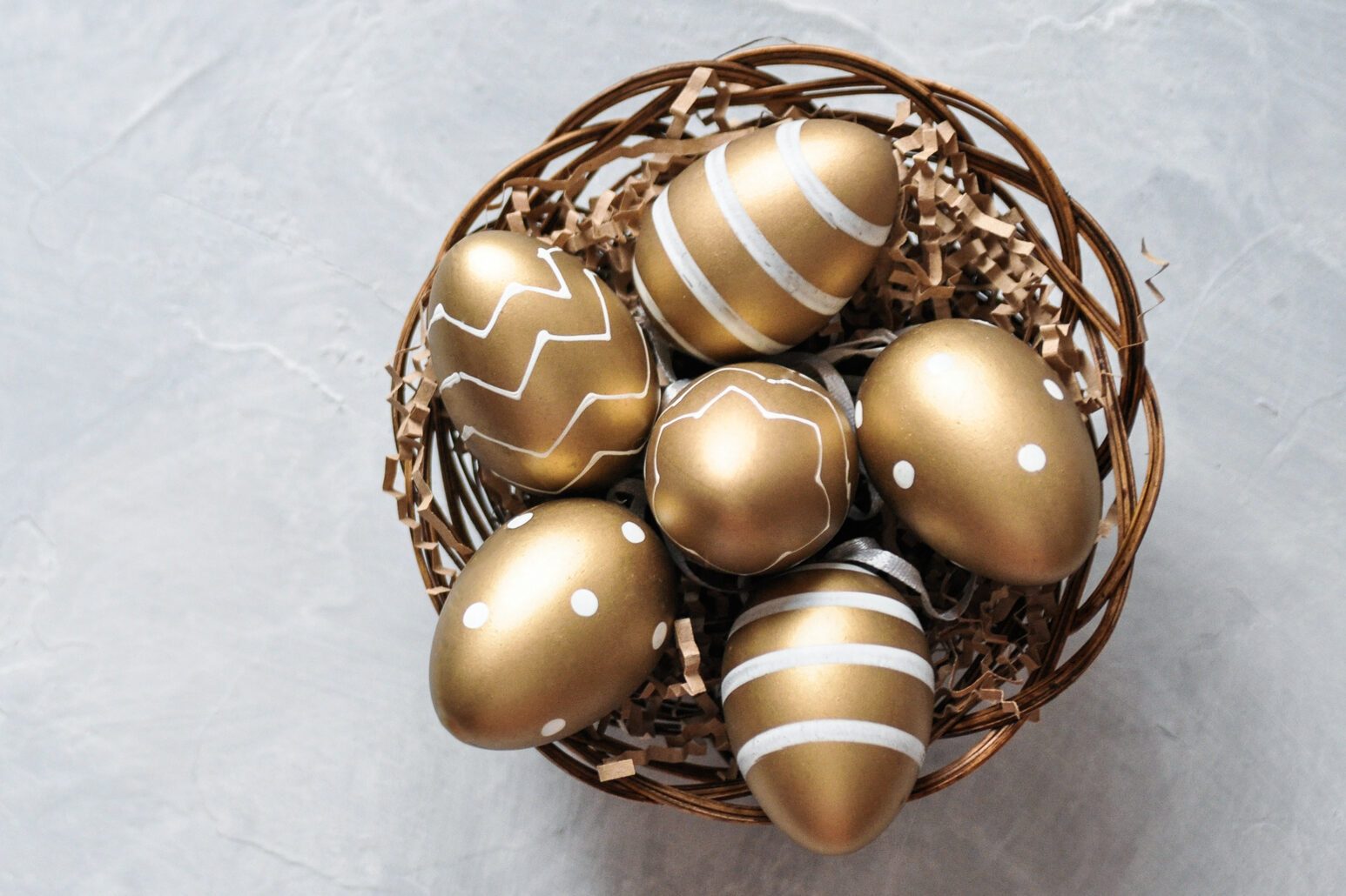 Easter decorative eggs in gold color with a pattern in a basket on a gray background