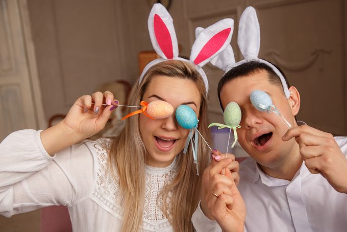 Happy Easter concept. Funny couple wearing bunny ears and having fun with Easter eggs at Easter day. Friends playing hunt eggs at Easter sunday