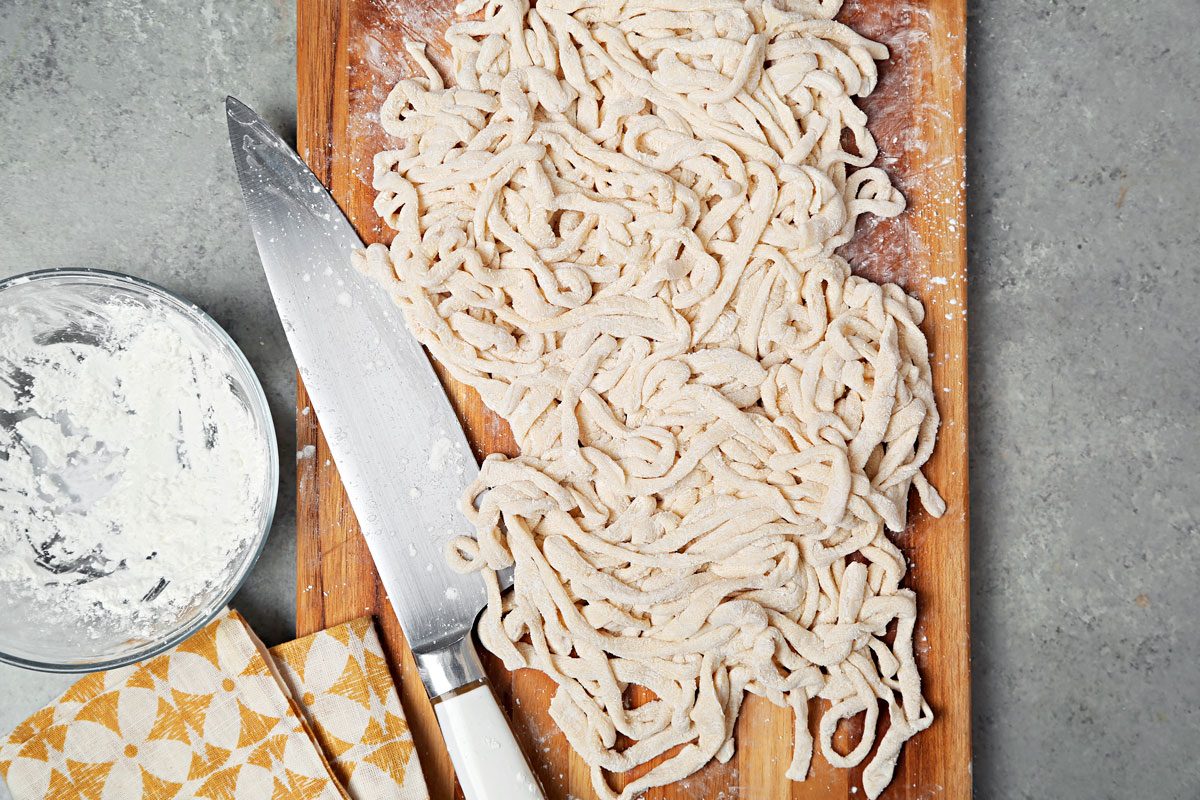 Shaped and sliced noodles tossed in cornstarch on a brown cutting board.