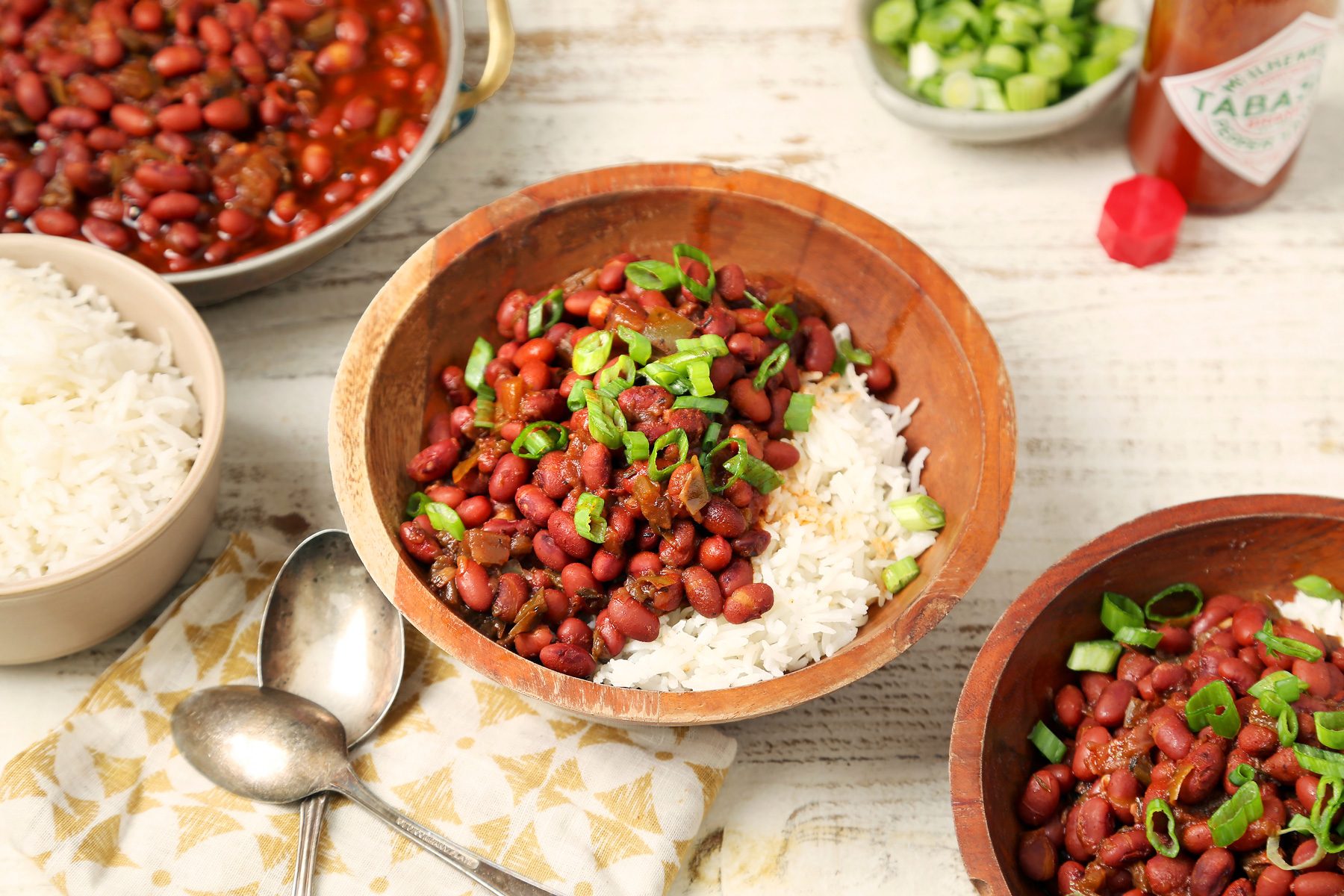 Taste of Home's Instant Pot Red Beans and Rice shot on a white wooden surface. Red beans served over rice with scallions and hot sauce.