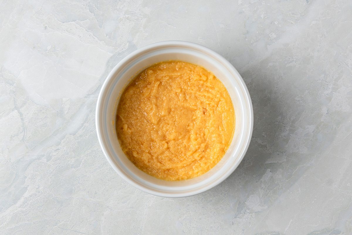 A bowl filled with creamy, yellow grits rests on a textured, light gray surface.