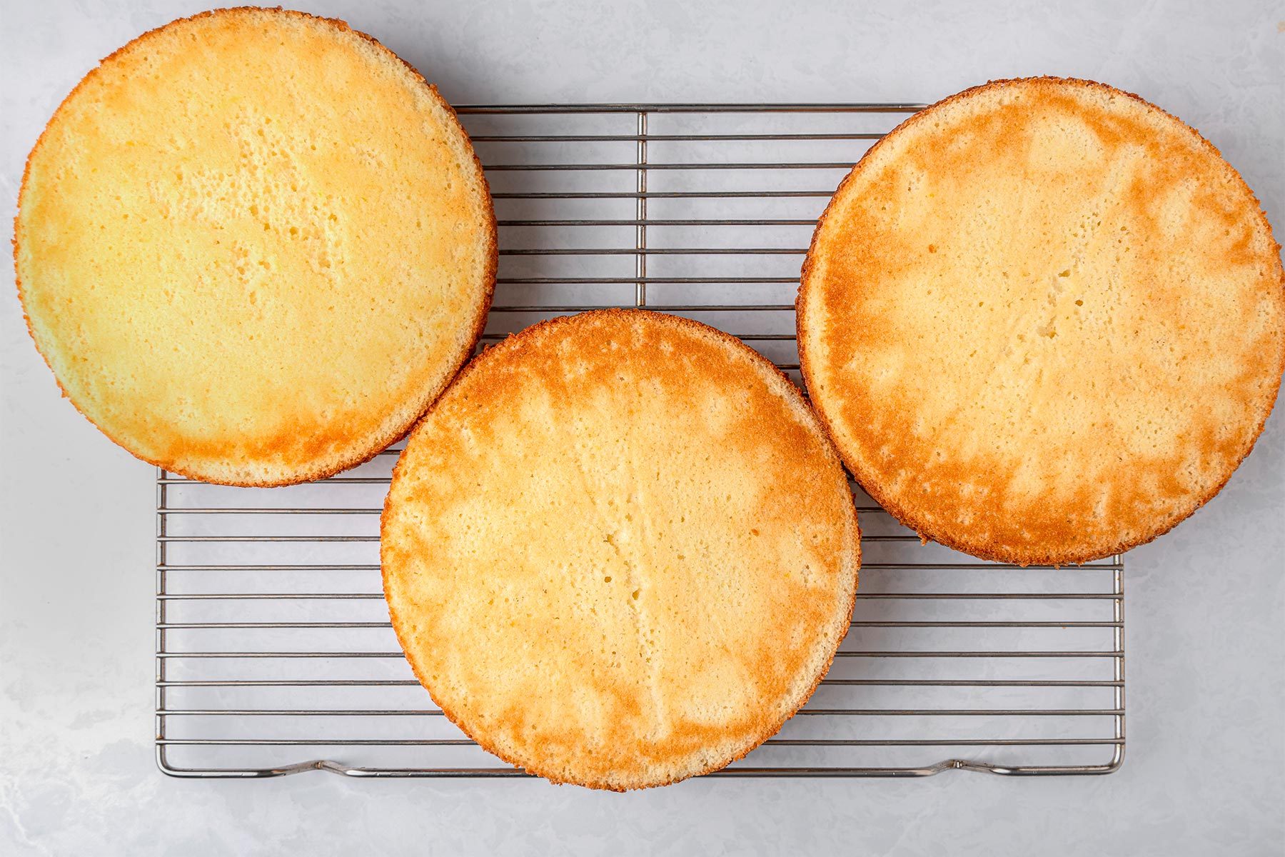Baked lemon cakes on a wired rack kept on top of a grey marbletop