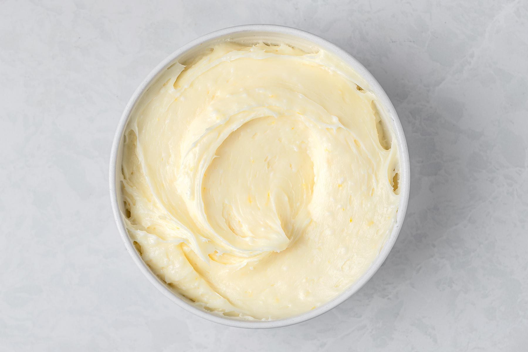 In a large bowl, beat cream cheese and butter kept on top of a grey marbletop.