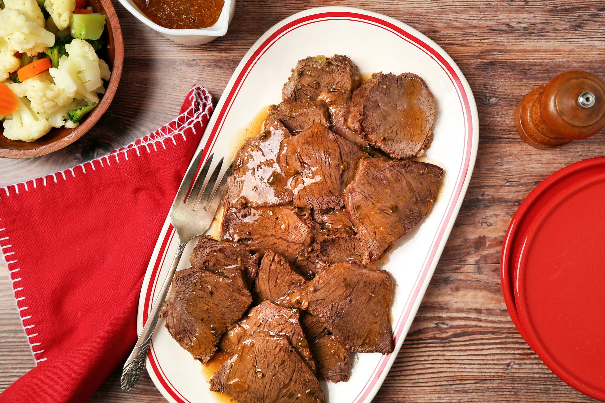 Marinated Pot Roast shot on a brown wooden surface. Sliced pot roast served on a platter with sauce; overhead
