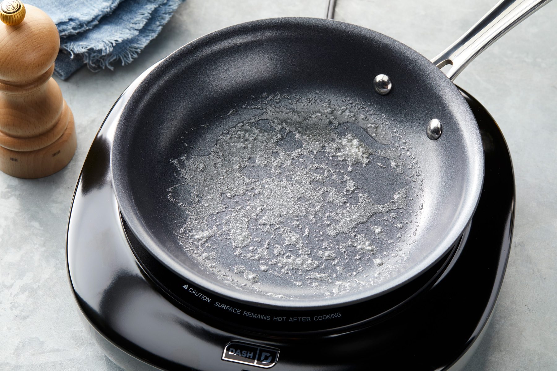 3/4 angle view shot of heat butter in a large skillet over medium heat; induction; napkin; grey surface;