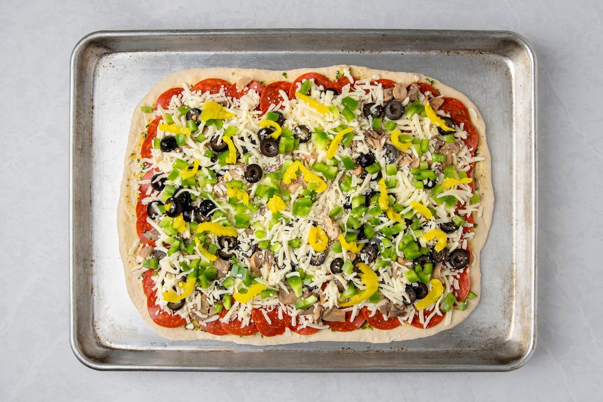 overhead shot of a pizza on a baking tray, the pizza is rectangular and features a visible crust edge, the baking tray is metallic and sits on a plain white background