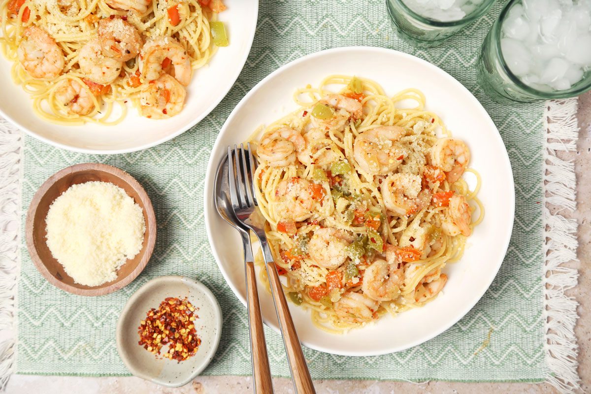 Shrimp Spaghetti shot on a beige marble surface. Pasta served in white bowls with parmesan and crushed red pepper flakes; overhead