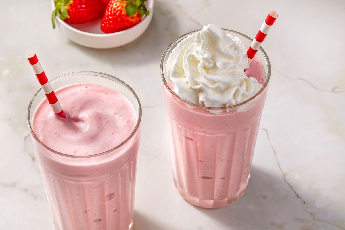 Close shot of Springtime Strawberry Malts; serve in a glasses; garnished with whipped cream; straws; a bowl of strawberry; marble surface;