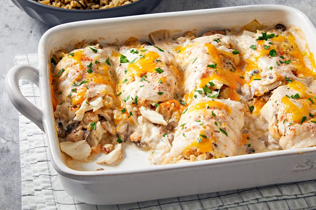 Casserole dish with stuffed sole topped with melted cheese and garnish, served on a textured cloth.
