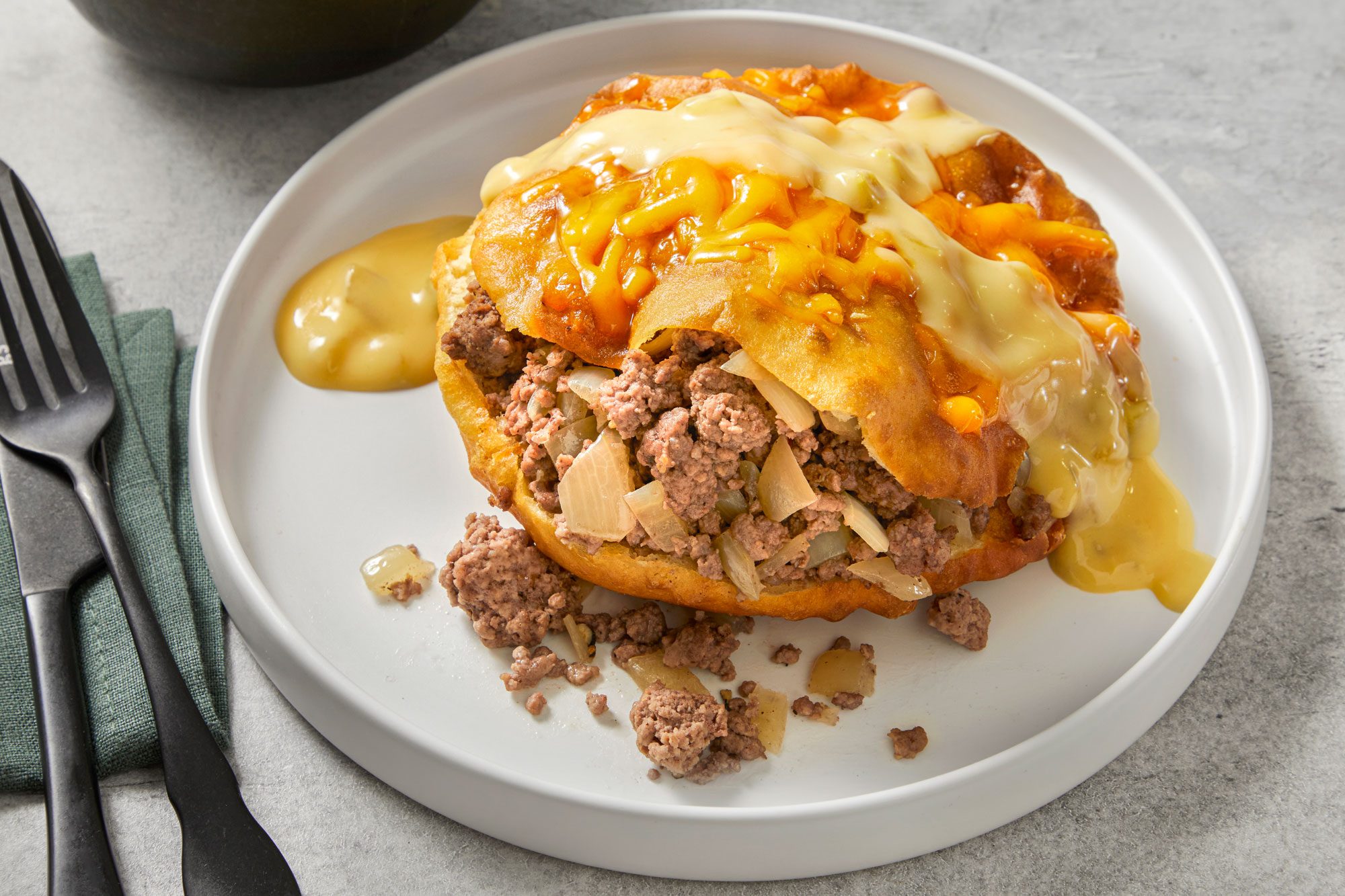 Close shot of Beef-Stuffed Sopapillas; top with cheese and serve on a plate with sauce; fork and knife; napkin, marble surface