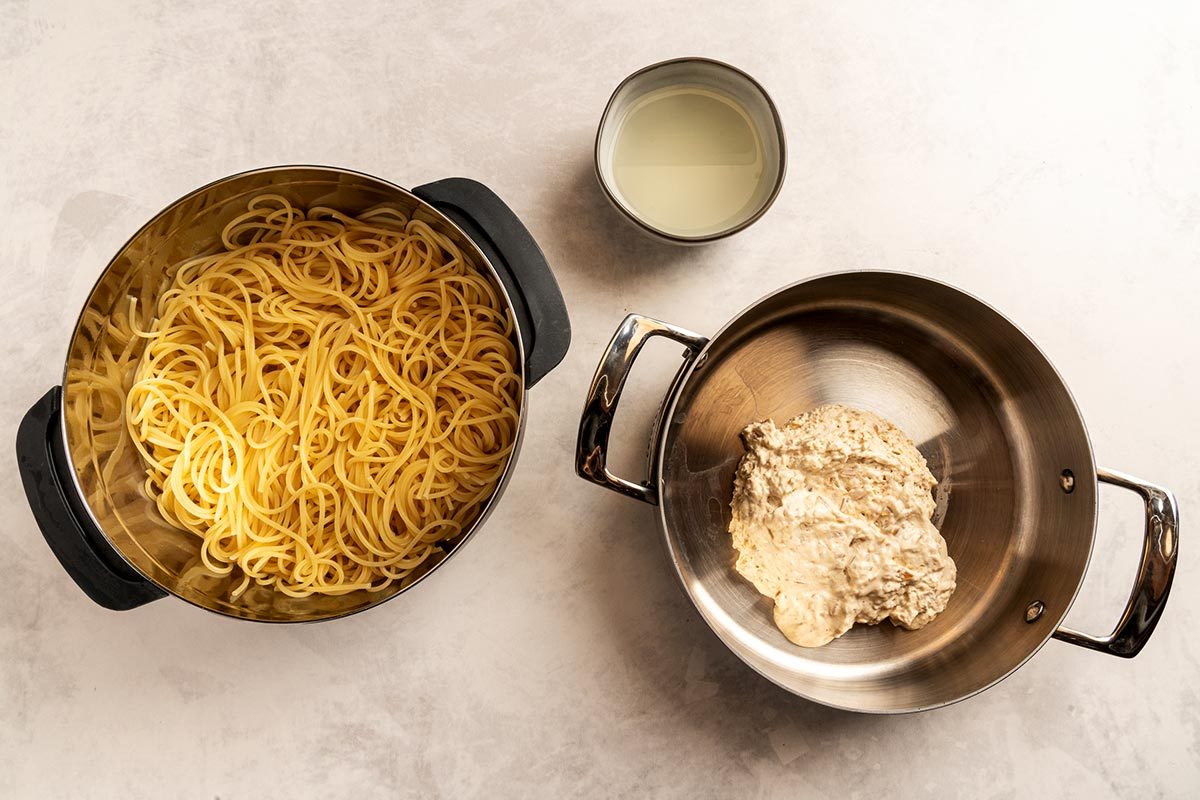 Pot of cooked spaghetti on the left, pot of caramelized onion dip on the right, with a small bowl of pasta water in between