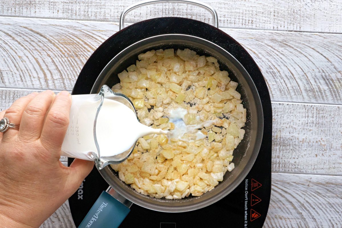 milk being added to sautéed onions and flour mixture