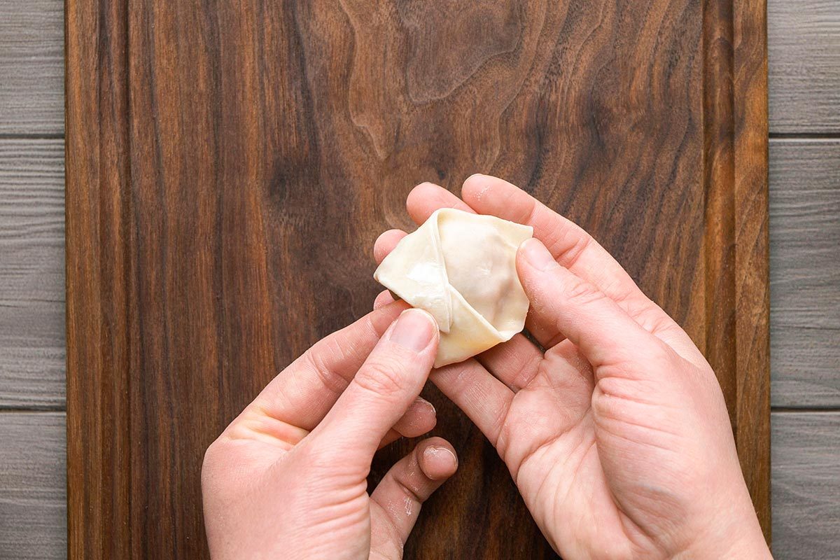 Wonton wrapper being folded in boat shape