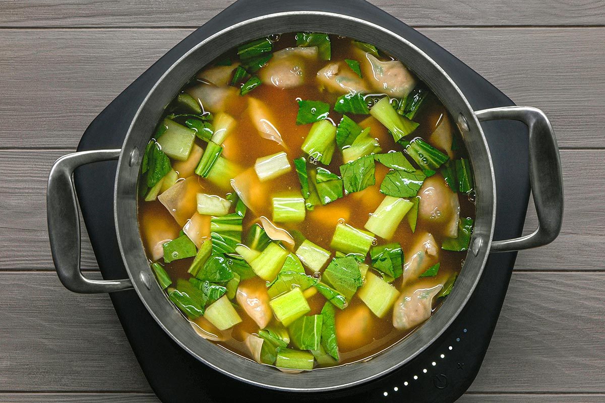 Wontons and bok choy are being heated in a pan for wonton soup
