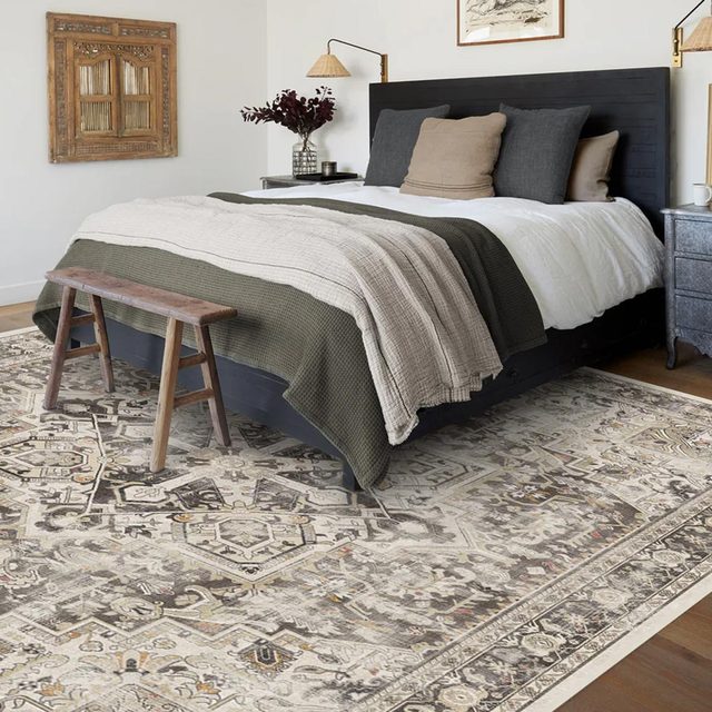 Black and gray area rug underneath a green and gray bed with wooden accents