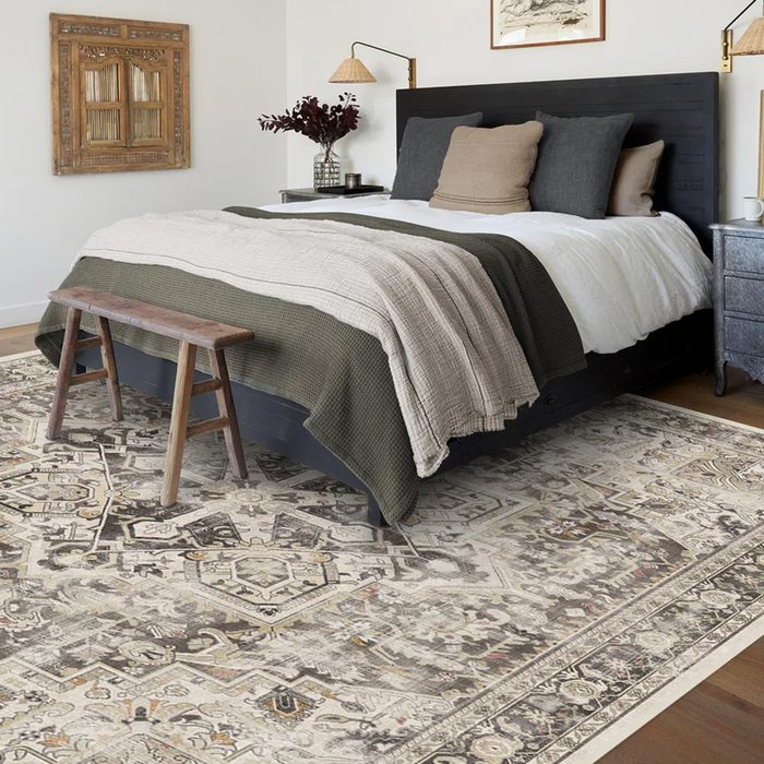 Black and gray area rug underneath a green and gray bed with wooden accents