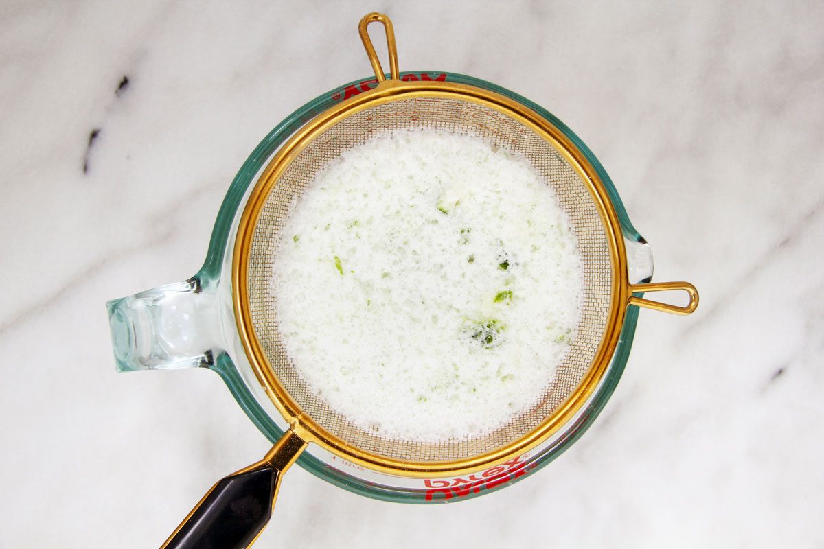 Top view of a clear measuring cup with a fine strainer resting on it.
