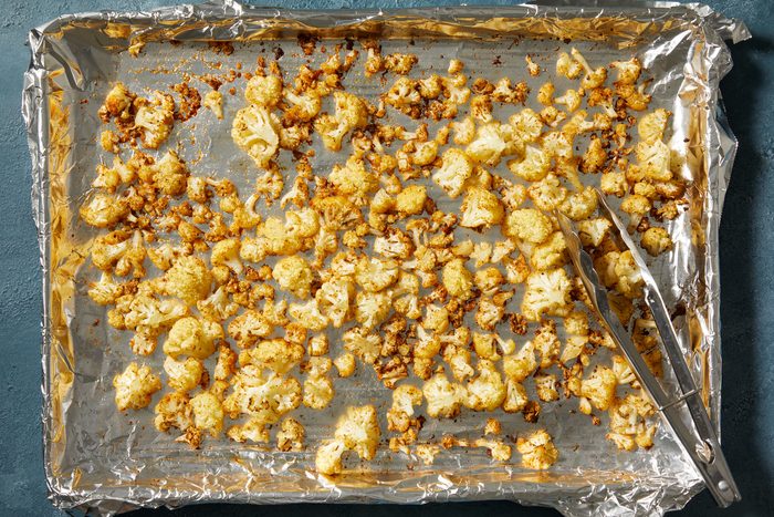 Overhead shot of Bake until cauliflower is tender and browned about 20 minutes; stirring halfway; tongs; dark blue surface;