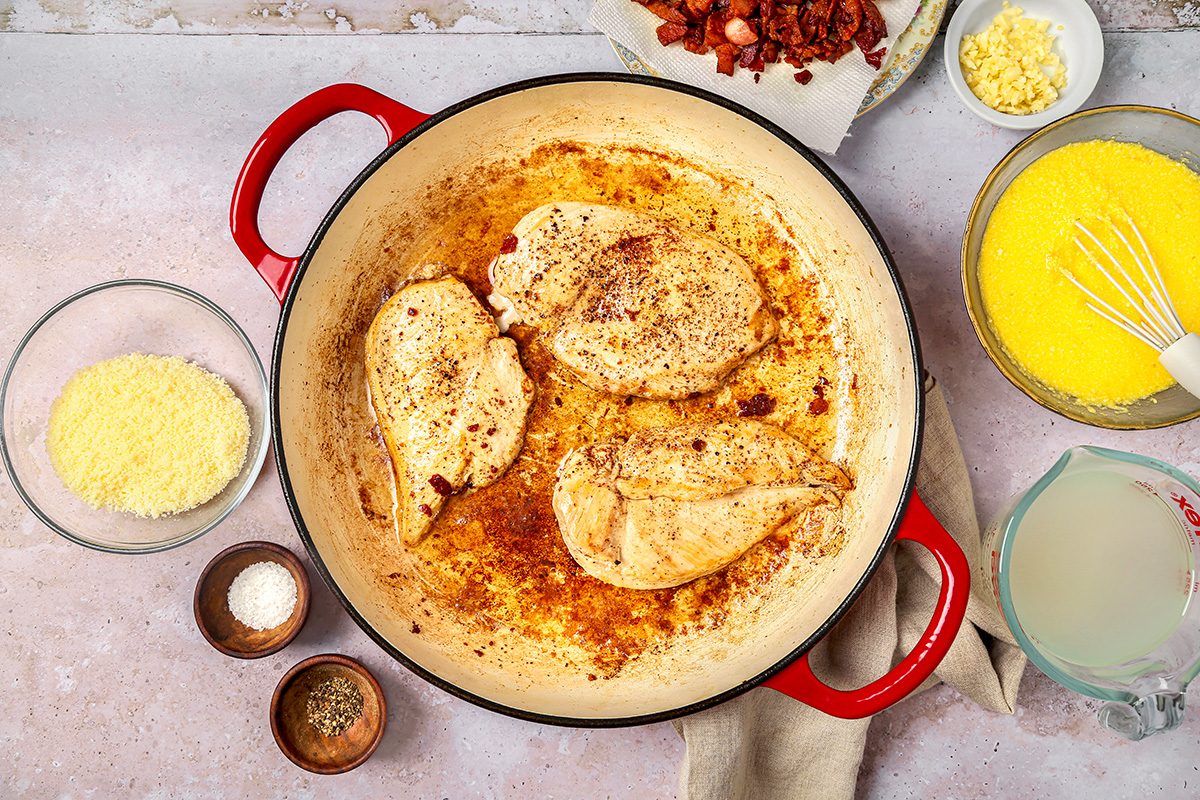 overhead shot of three cooked chicken breasts seasoned with spices, sitting in a light brown sauce at the bottom of the pot