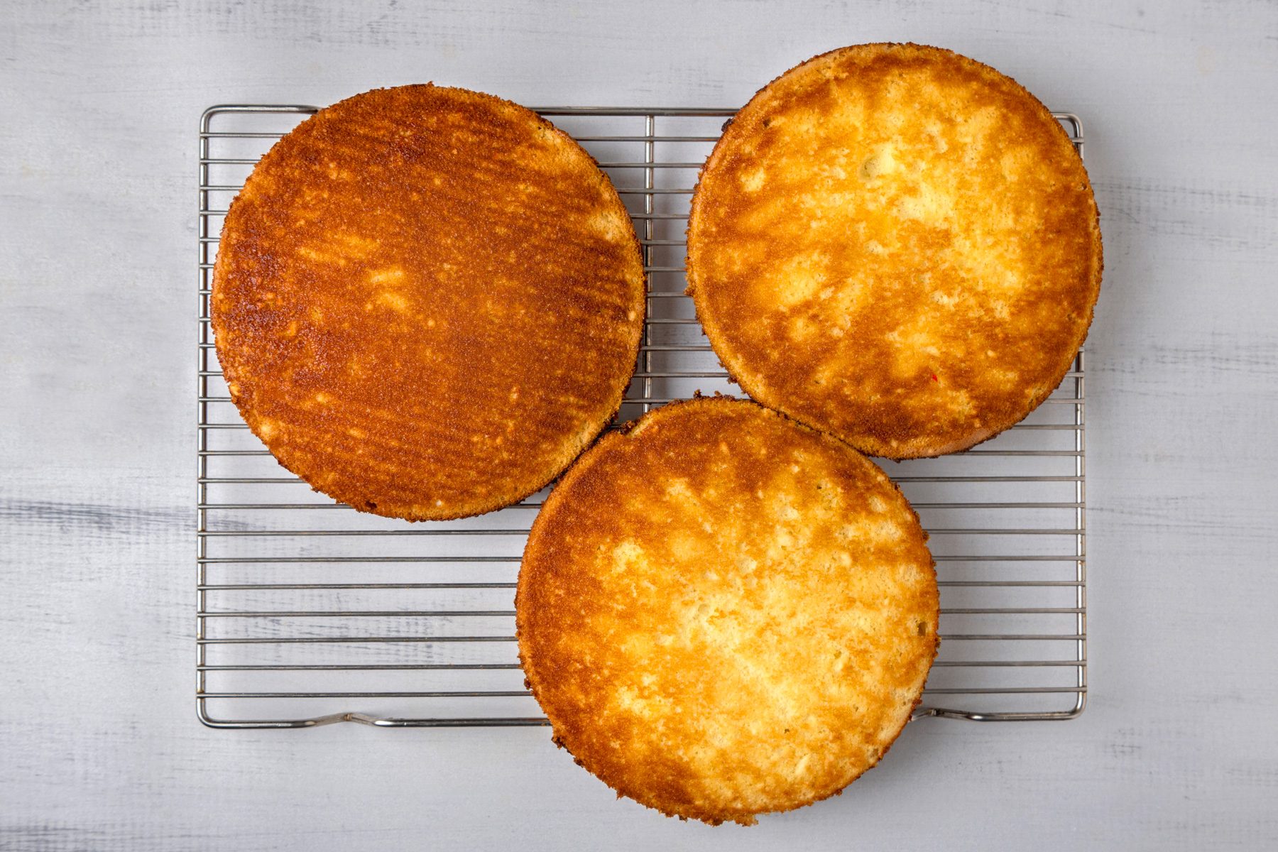 overhead shot of three round cake layers cooling on a wire rack; the wire rack is positioned on a light colored surface