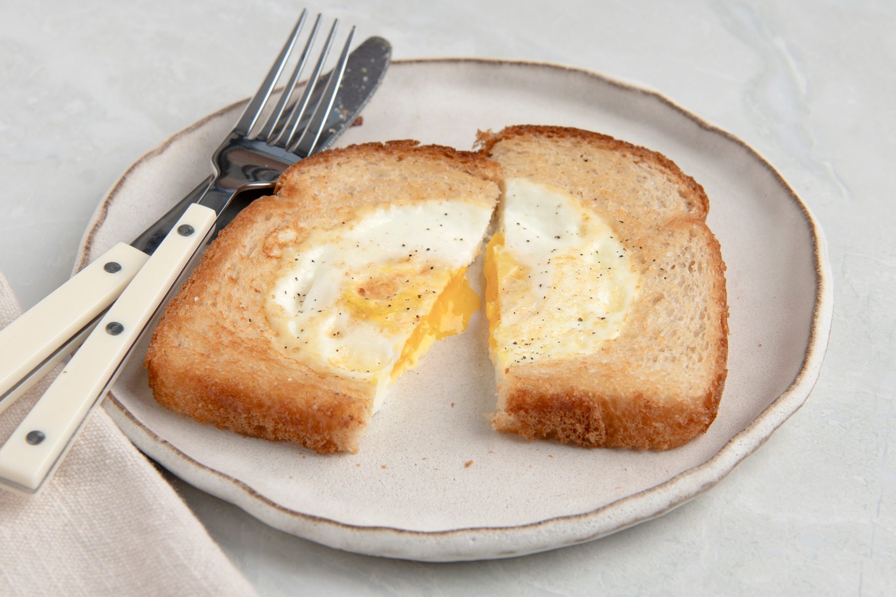 Close view shot of Toad in the Hole; served ona ceramic plate; season with salt and pepper; fork and knife; a napkin; on marble surface;