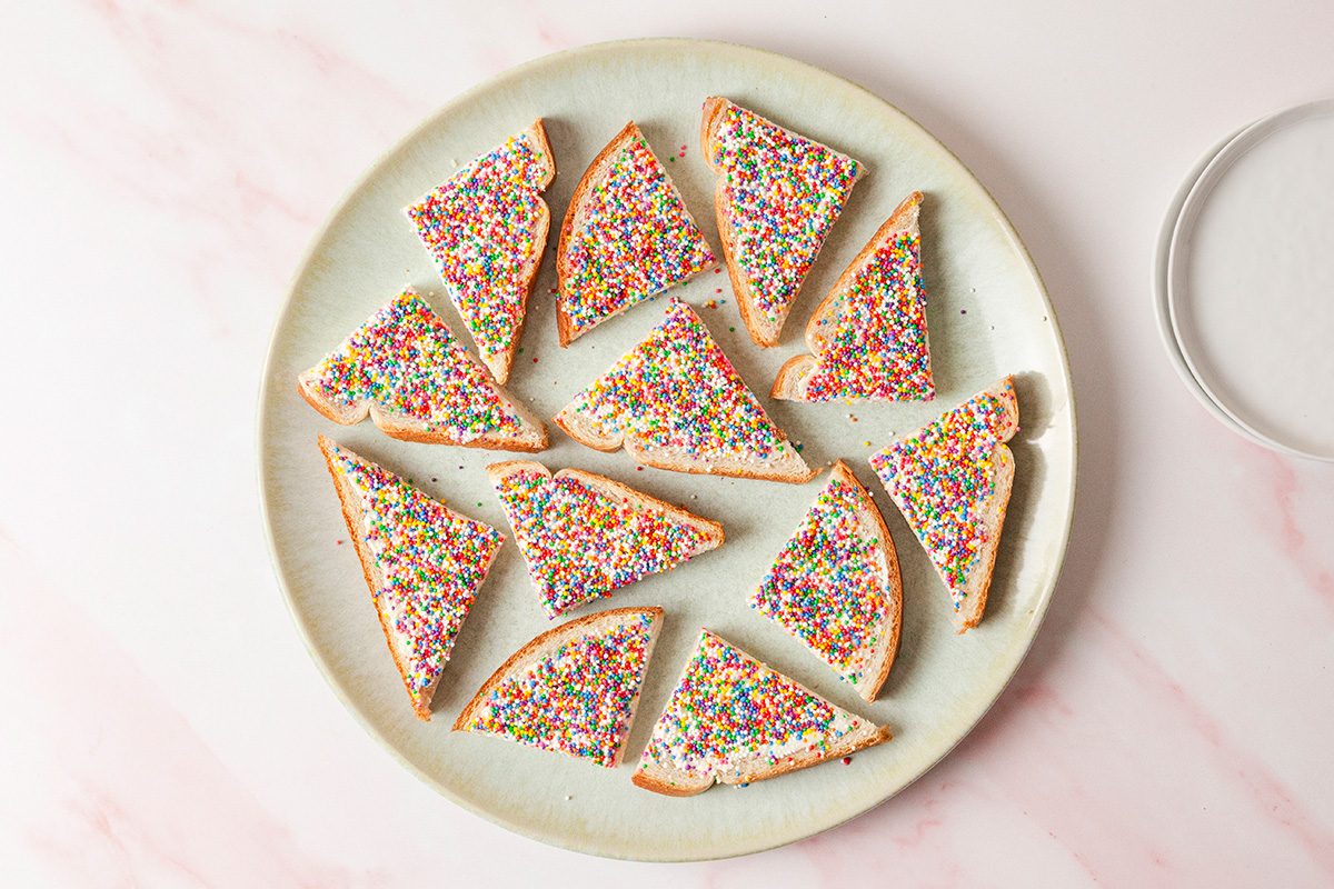 A plate of triangular bread slices topped with colorful sprinkles on a light pink marble surface.