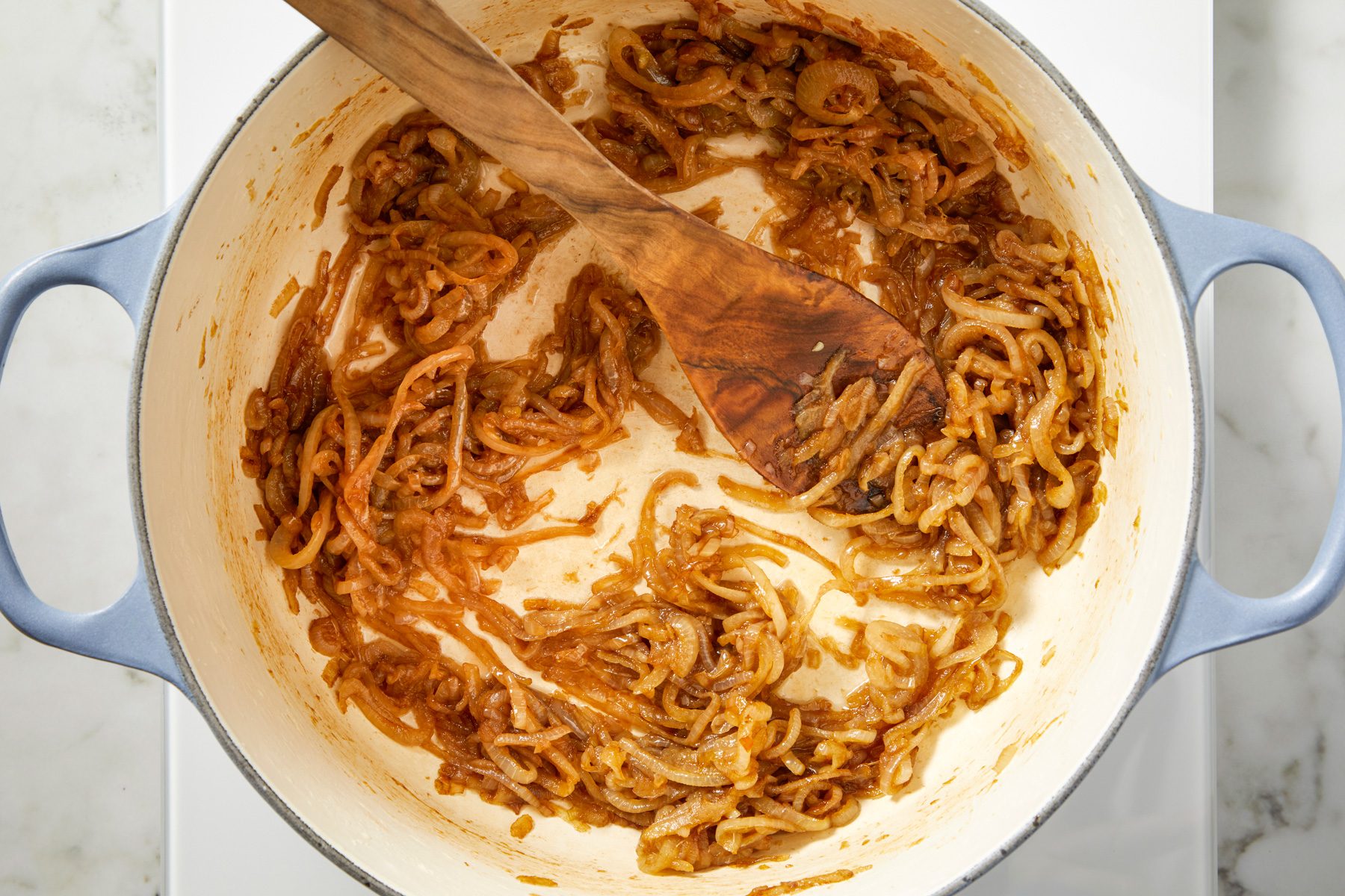 A pot with olive oil, butter, and thinly sliced onions being cooked on medium heat, with a pinch of salt added, slowly caramelizing to a deep brown color.