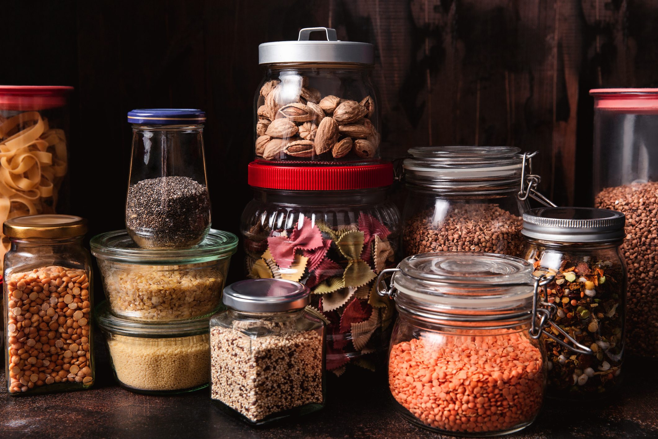 Various seeds in storage jars in pantry, dark textured background