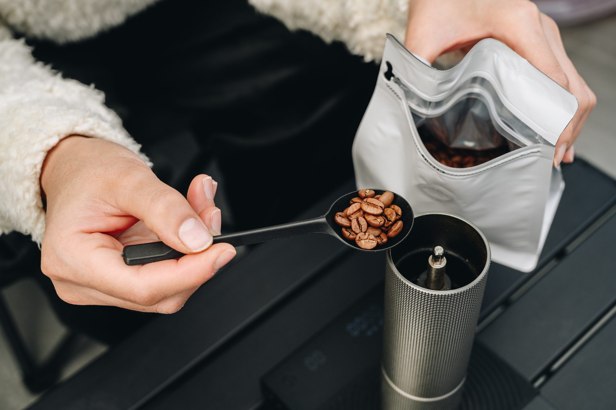 Cropped shot of barista while adding coffee beans into manual coffee grinder.