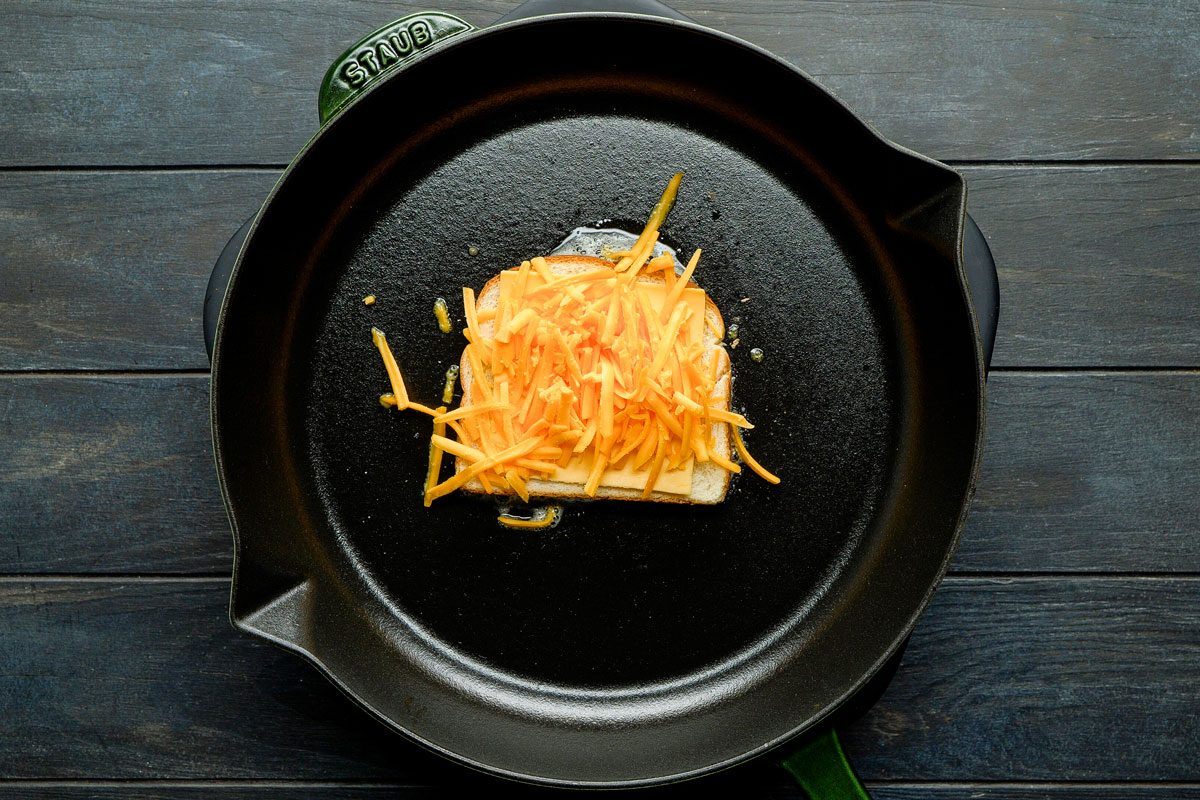 Place a slice of American cheese on bread and divide shredded cheddar cheese on top
