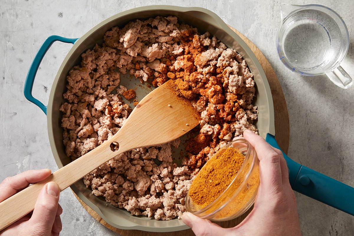 overhead shot of a large, shallow pan filled with cooked, crumbled meat, of ground turkey with various spices sprinkled over it