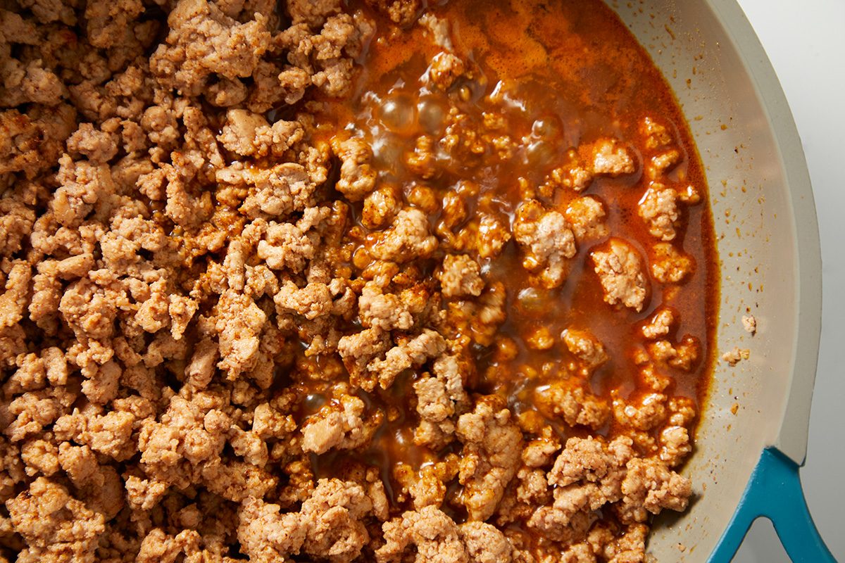 a closeup view of cooked ground meat in a skillet, featuring a mixture of crumbled light brown meat and a rich, reddish brown sauce that pools beneath it