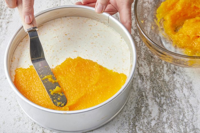 Spreading mango mousse on top of the cooled cake with the help of a spatula