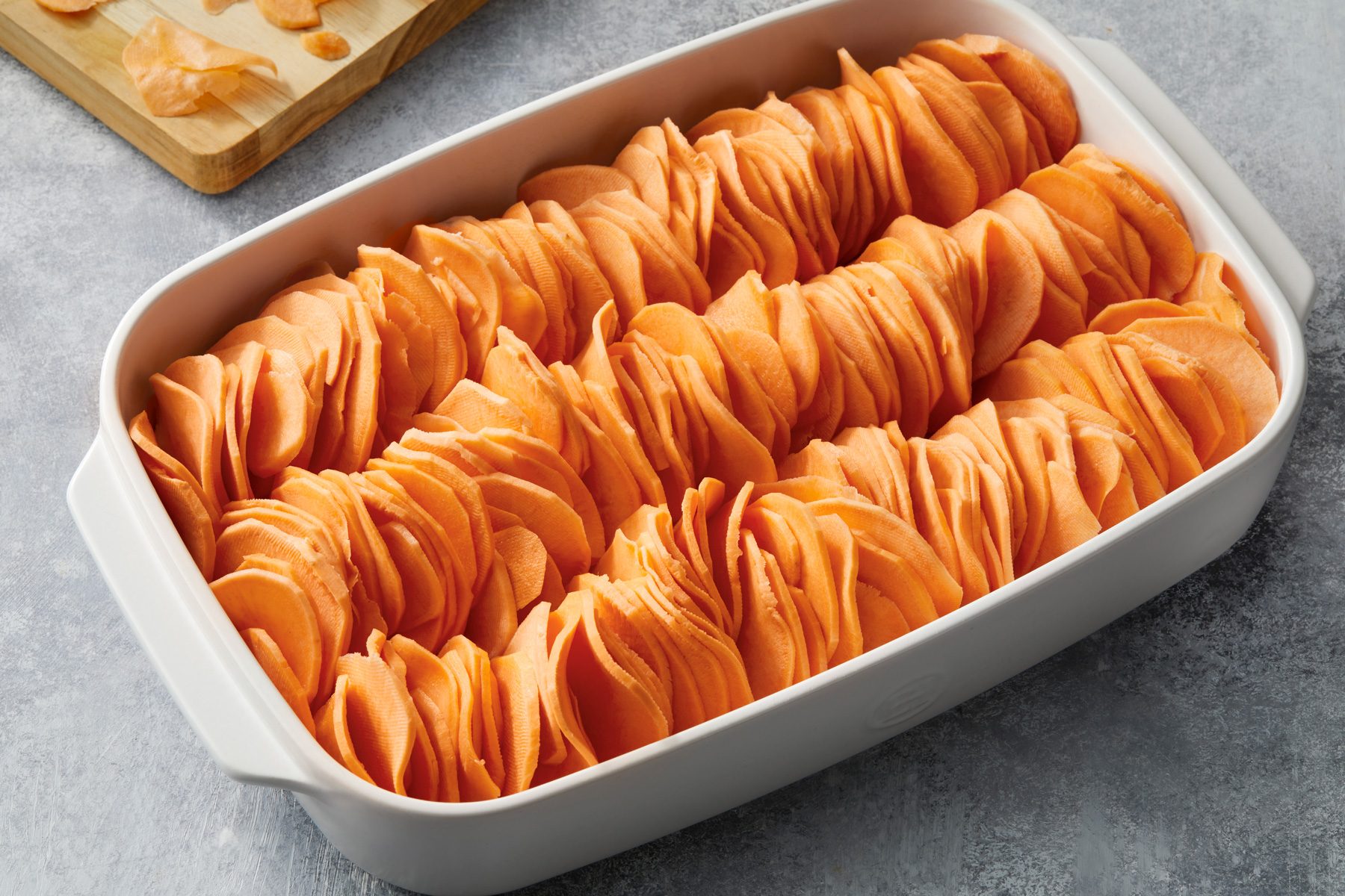 High angle view shot of a greased 13x9-inch baking dish arrange sweet potato slices in rows; set aside; Preheat oven to 400 degree; grey surface