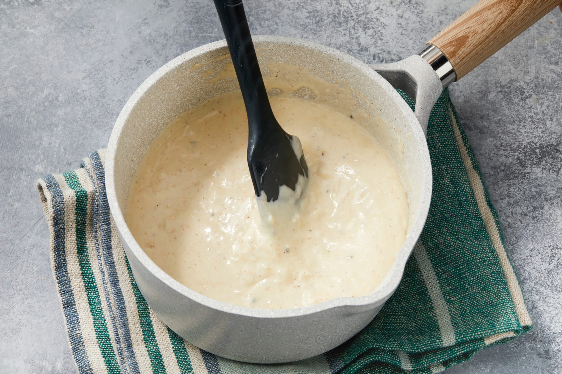 Overhead shot of the same saucepan; remove from heat; using spatula and stir until cheese is melted; placed over a napkin; on a grey surface;