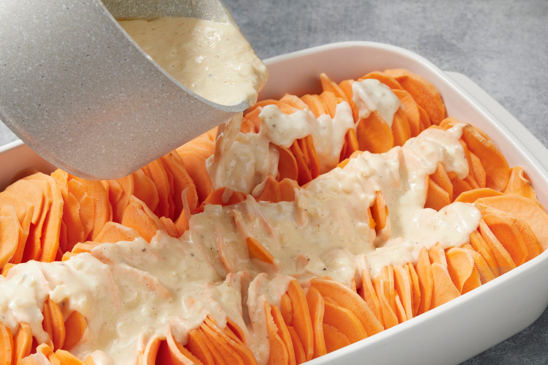 Close shot of pour cheese sauce over sweet potatoes; on grey surface;