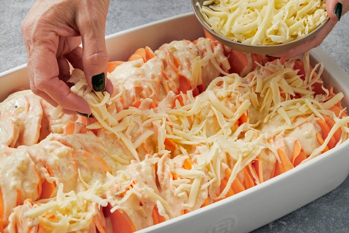 Close up shot of sprinkle remaining 1 cup Gruyere on top; Bake covered 30-35 minutes; Remove covering; bake until cheese is bubbly and golden brown on top 10-15 minutes longer; Let rest 10 minutes before serving; all set on a grey surface