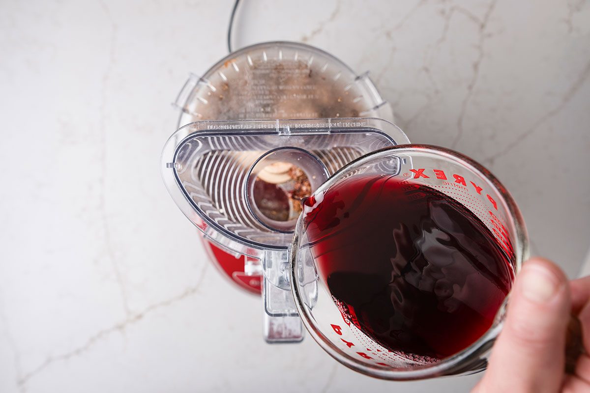 Red wine pouring to the drid fruits in processor