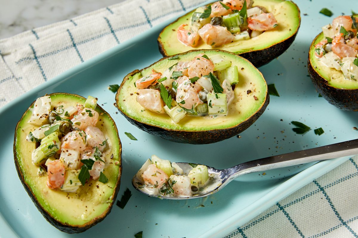 Top view shot of Shrimp Salad-Stuffed Avocados; garnish with additional parsley and serve immediately; spoon; napkin; all set on marble surface;