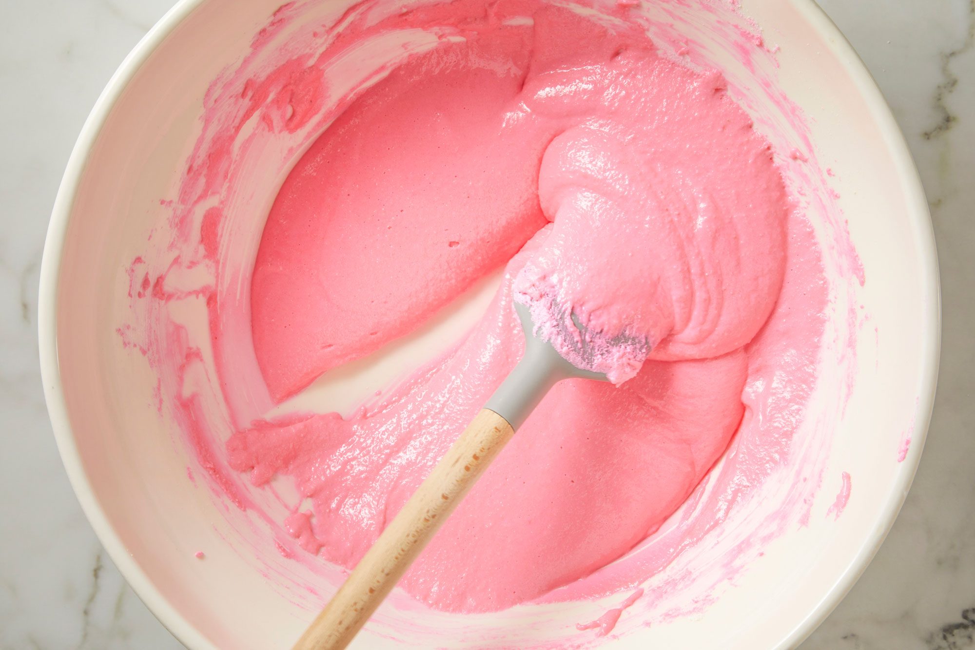 Close shot of run spatula down the center of the bowl; the line in the batter should remain visible for a moment before mixture runs back into itself; on marble surface;
