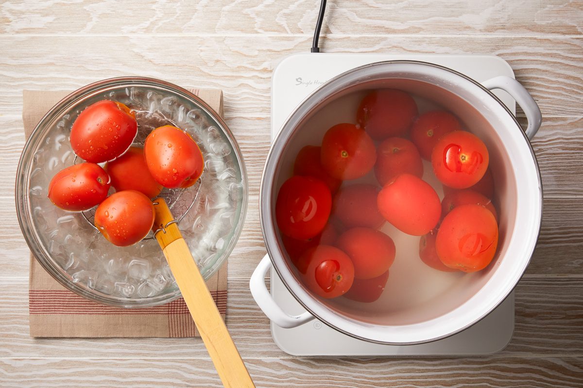 tomatoes being scooped out with a large slotted spoon and placed in the ice water bath